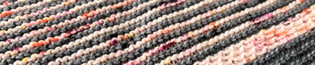 Close up shot of a striped, knitted shawl comprising of grey and cream stripes with specks of neon orange and pink.