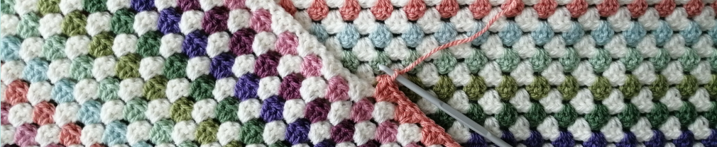 Close up of a crocheted blanket comprising stripes of coral, pink, mauve, purple, green, lime, pale mint, duck egg blue and cream.