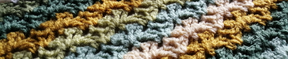 Close up of crochet blanket featuring stripes of a flower motif in cream, mustard, and shades of green.